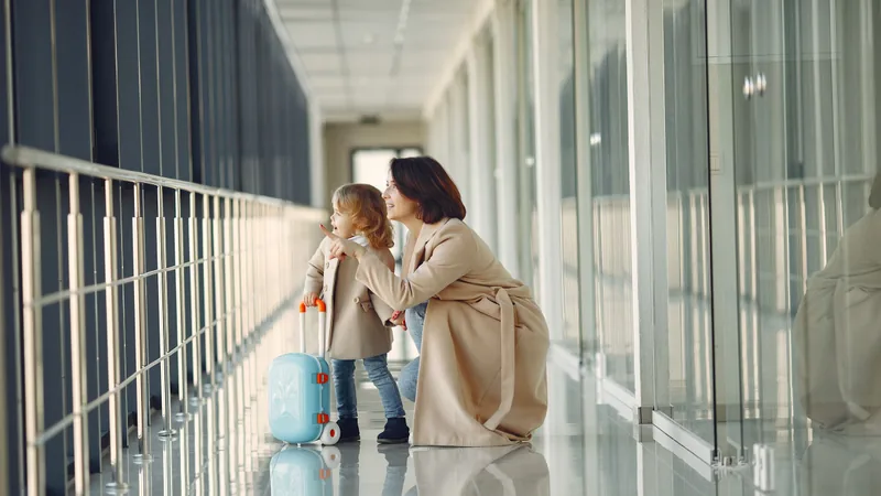 A mother and daughter looking out of an airport window with their suitcases.